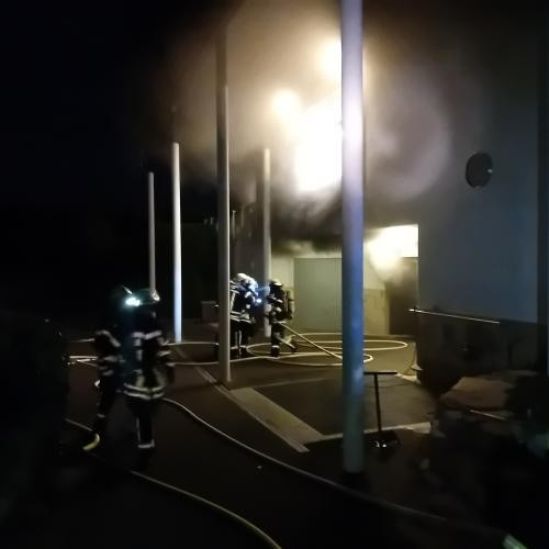 Schwarzer Rauch kommt aus dem Gebäude 4 Feuerwehrmänner stehen daneben